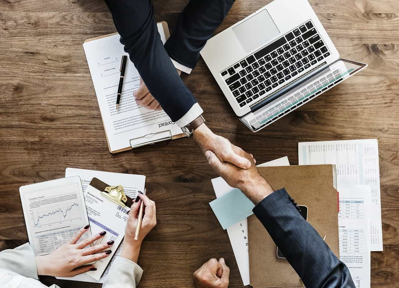 A pair of hands shake over a desk.