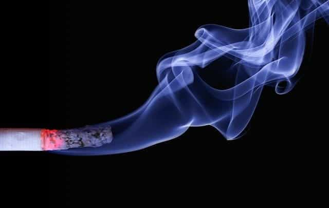 A lit cigarette smoking in front of a black background.