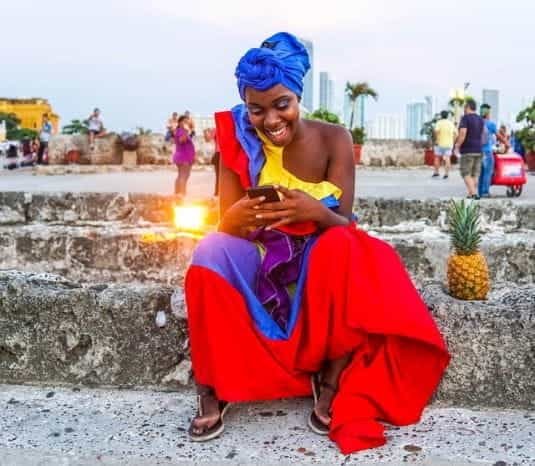 A woman in a brightly colored outfit in Cartagena, Colombia looks at her phone.