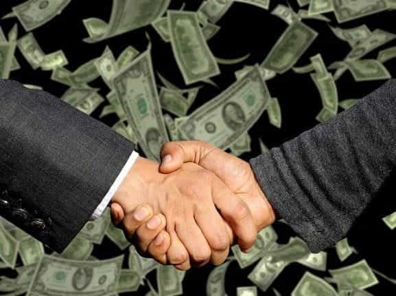 A handshake taking place on a background of flying US Dollar bills.