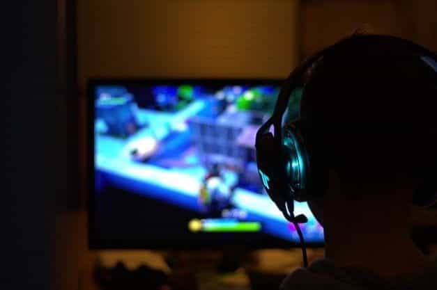 The silhouette of the back of a person while they play a videogame with a headset on.