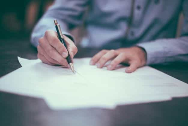 Hands sign paperwork at a desk.