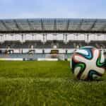 A football on a grass pitch in a stadium.