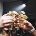 A group of people holding up shot glasses of alcohol in a bar.