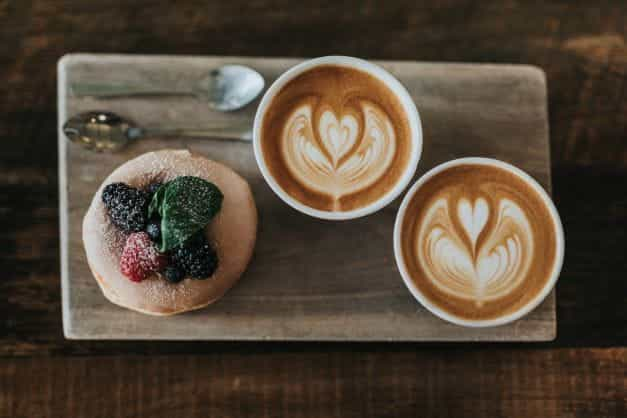 A puff pastry and two coffee mugs placed on a wooden serving tray.