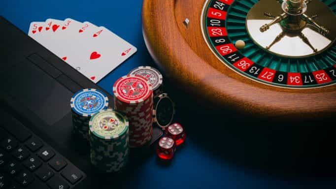 Poker chips, playing cards, and a roulette wheel placed on a table next to a keyboard.