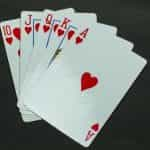 Five playing cards in the same suit of hearts lying flat on a grey surface.