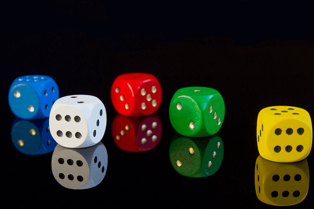 Four die, each one in a different color, laying on a black reflective surface against a black background.