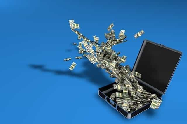 Large amounts of US dollar cash bills flying out of an open briefcase on a blue background.