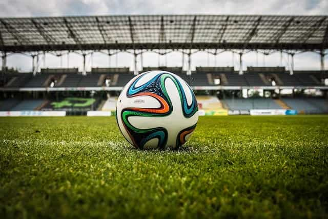 A football on a grass pitch in a stadium.