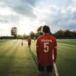 Men stand around a sporting field in jerseys.