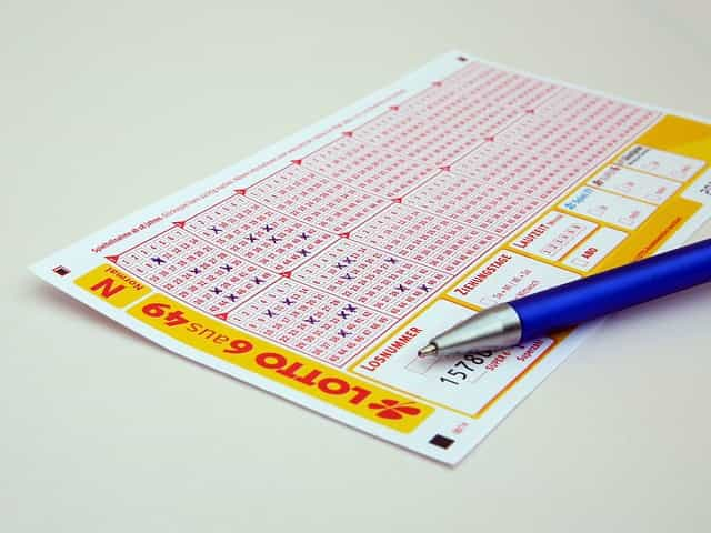 A lottery playing card lying flat on a table with a pen placed on top of it.