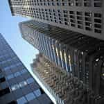 A low-down, ground level shot looking upwards at several tall skyscrapers in the middle of a city’s downtown district.