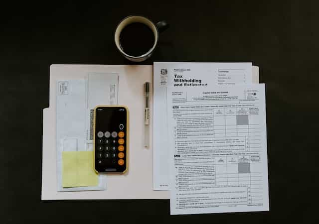 A worktop from above with various tax paperwork, a calculator and a cup of coffee.