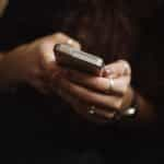 Both of a woman’s hands holding a smartphone while typing on it.