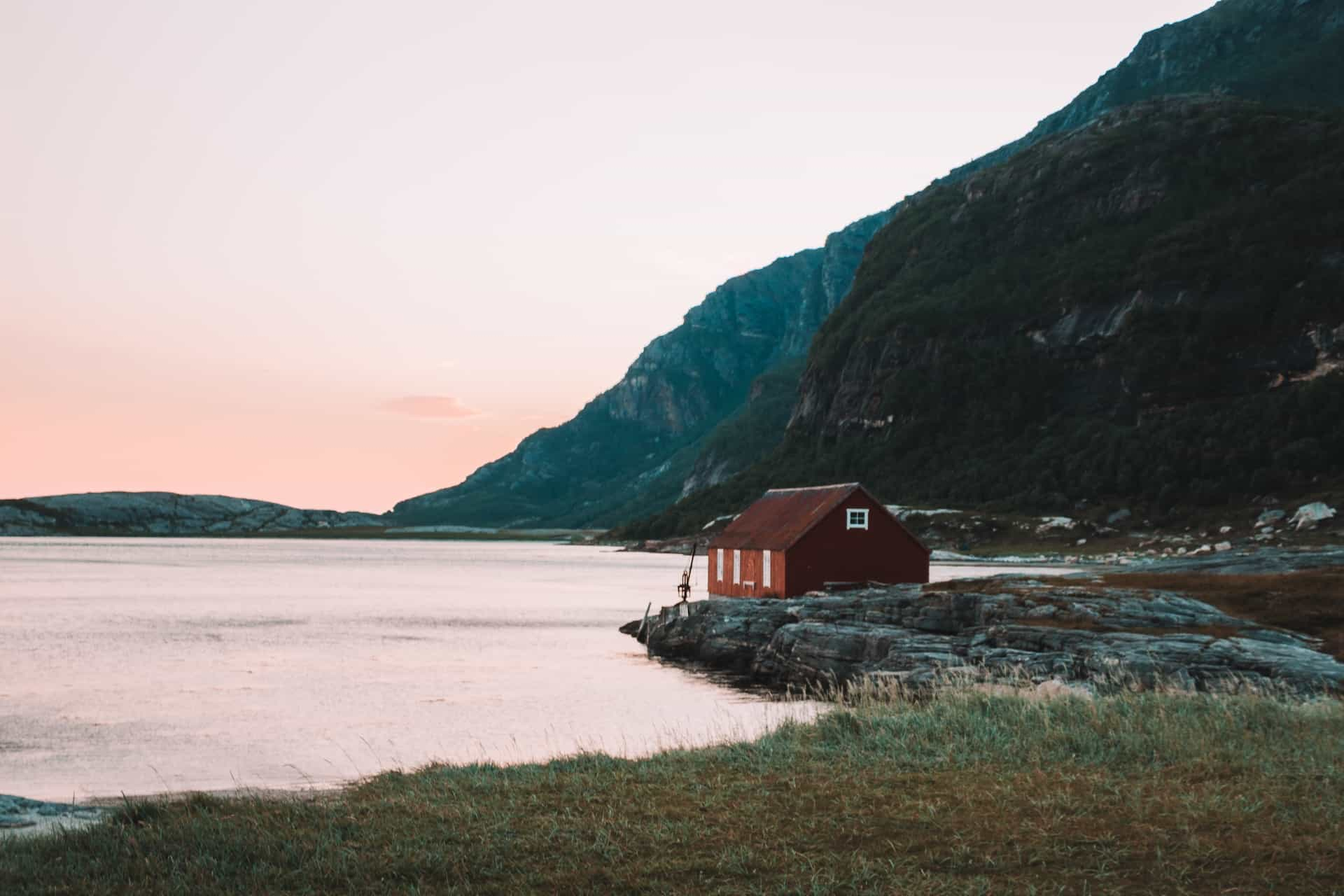 A reddish brown house beside body of water near a mountain.