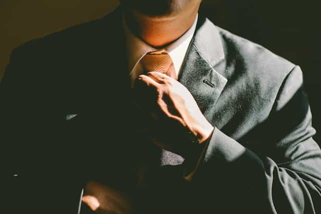 A man in a suit straightening his tie with the sun illuminating part of his suit.