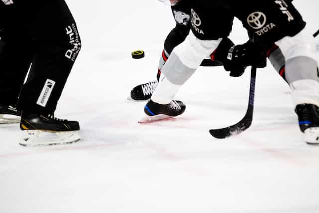 Several hockey players vying for control of the puck on an ice rink during a game of hockey.