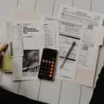 Documents and calculator on phone kept on wooden floor.