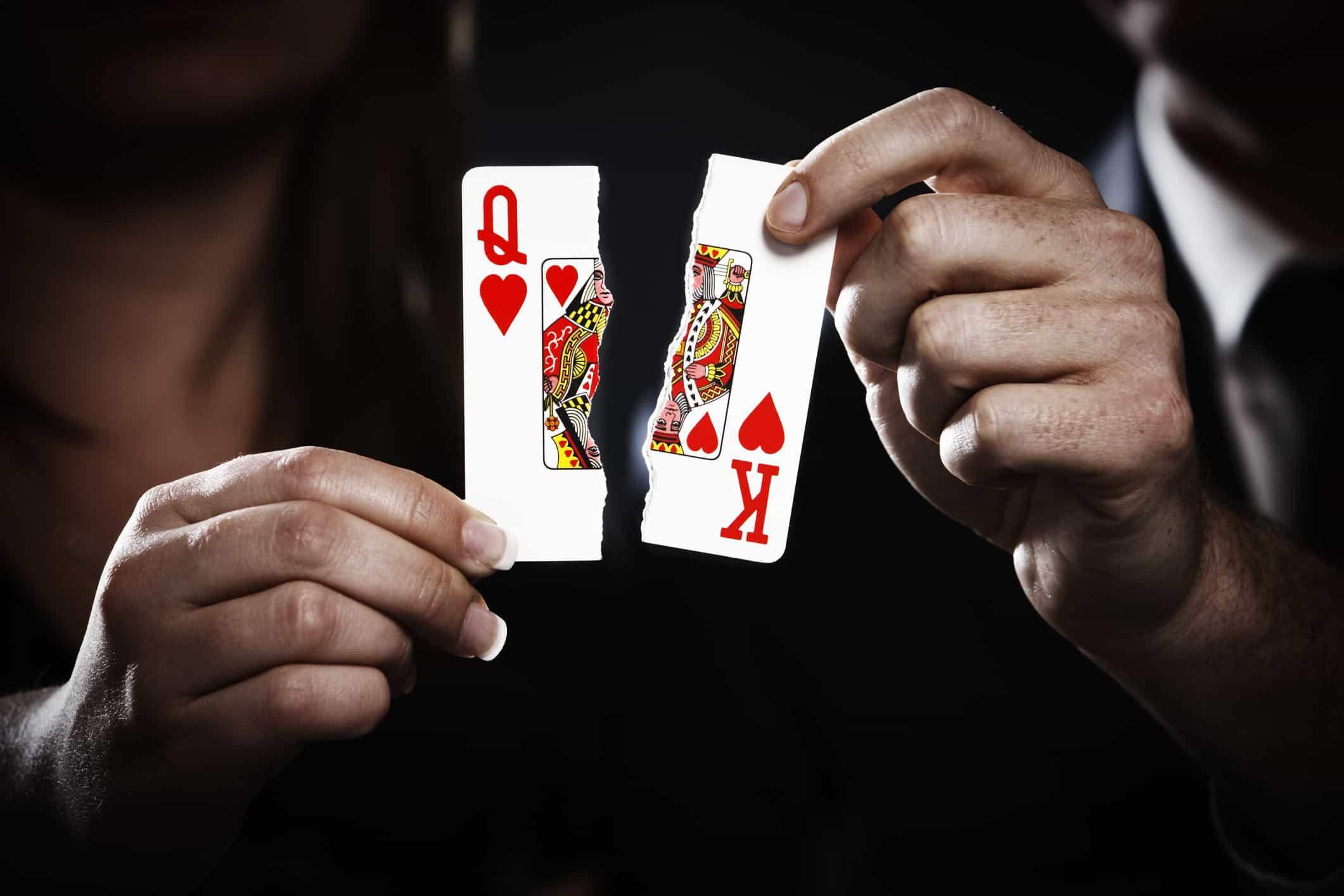 Playing cards, a Queen and King of Hearts, are torn in two.