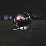 The helmet of an American football player sitting on the field with two teams seen off in the background.