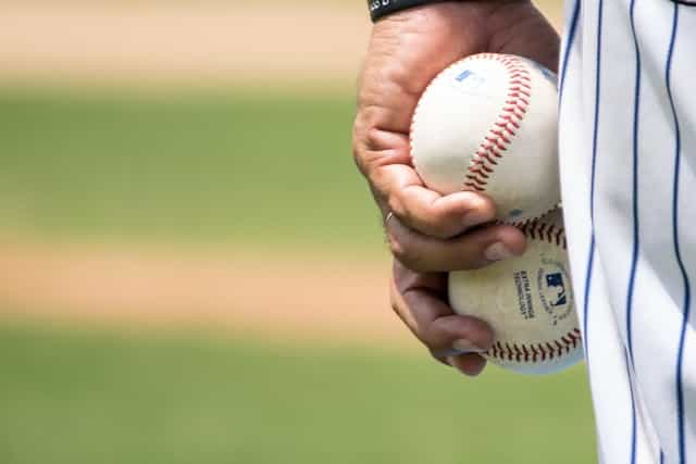 A pitcher at a baseball game holding two baseballs in his left hand as he prepares to throw one at the batter.